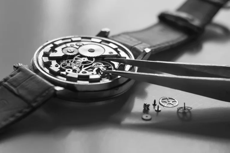 Montre mécanique ouverte, pinces manipulant rouages, précision et minutie horlogère.