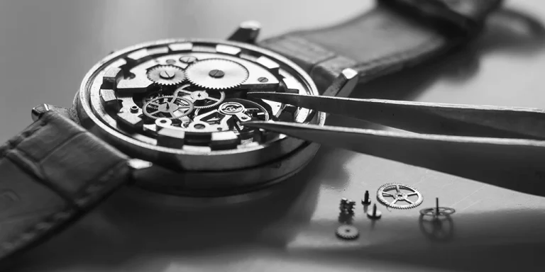 Montre mécanique ouverte, pinces manipulant rouages, précision et minutie horlogère.